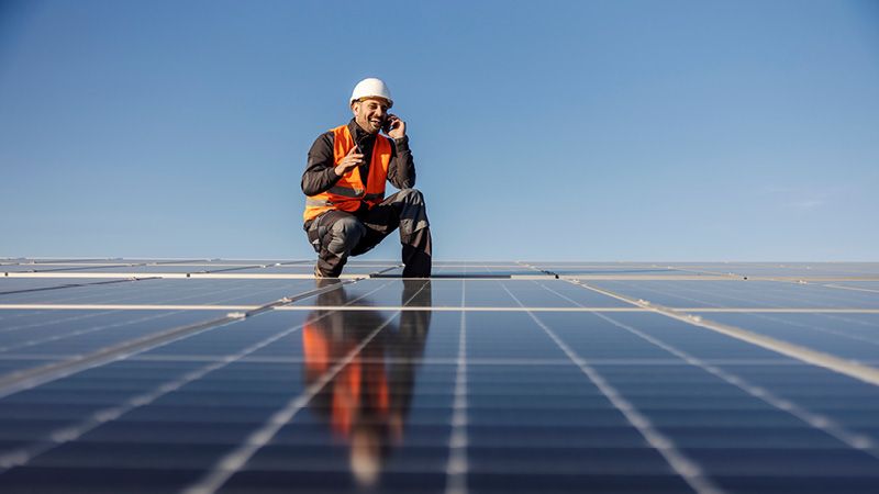Handwerker hockt auf Dach mit Solarmodulen