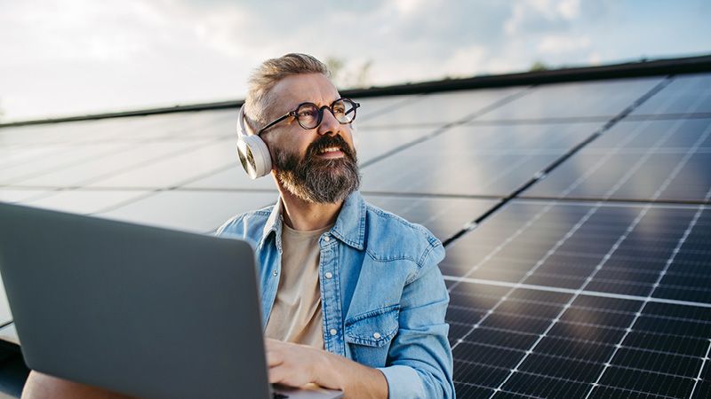 Mann mit Laptop auf Dach mit Solarmodulen